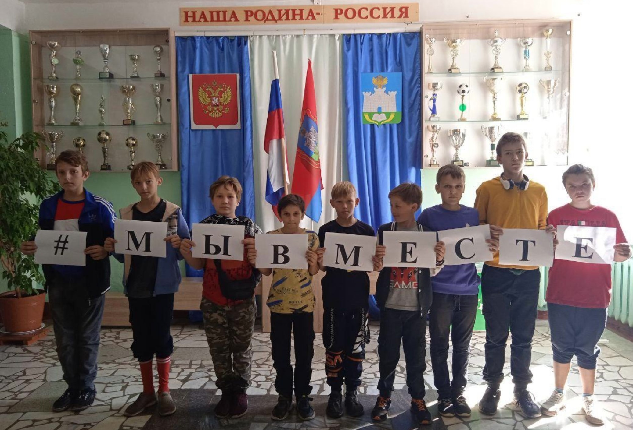 Children at a Russian school orphanage, likely including those forcibly abducted from Ukraine, holding the pro-war slogan (we’re together) and under a sign claiming that ’Russia is our motherland’