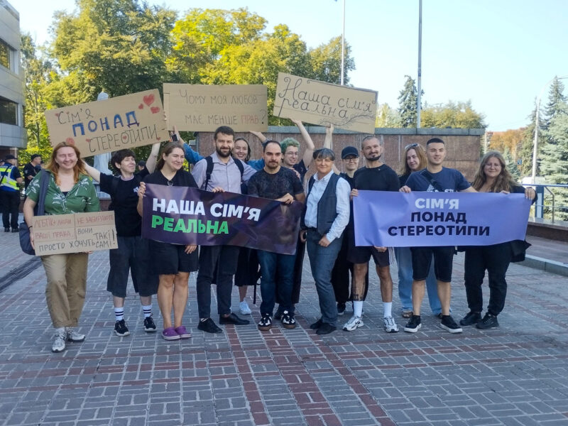 Tymur Levchuk, Zoryan Kis and Oksana Huz, surrounded by activists. The placards say, for example, ‘Our family is real’ and ‘Family over stereotypes’ Photo Mykhail Tiunkin, Graty