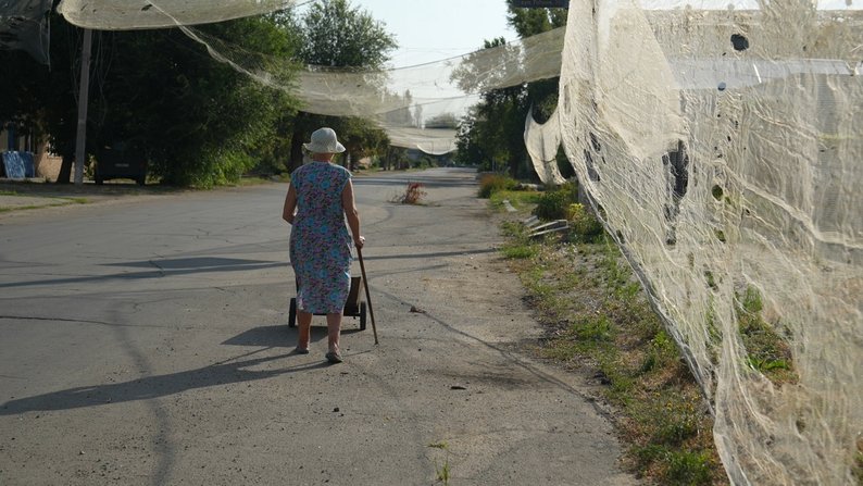 Липень 2025 року. Оріхів, Запоріжжя. Місцева мешканка йде під антидроновими сітками. Фото: “Суспільне Запоріжжя”.